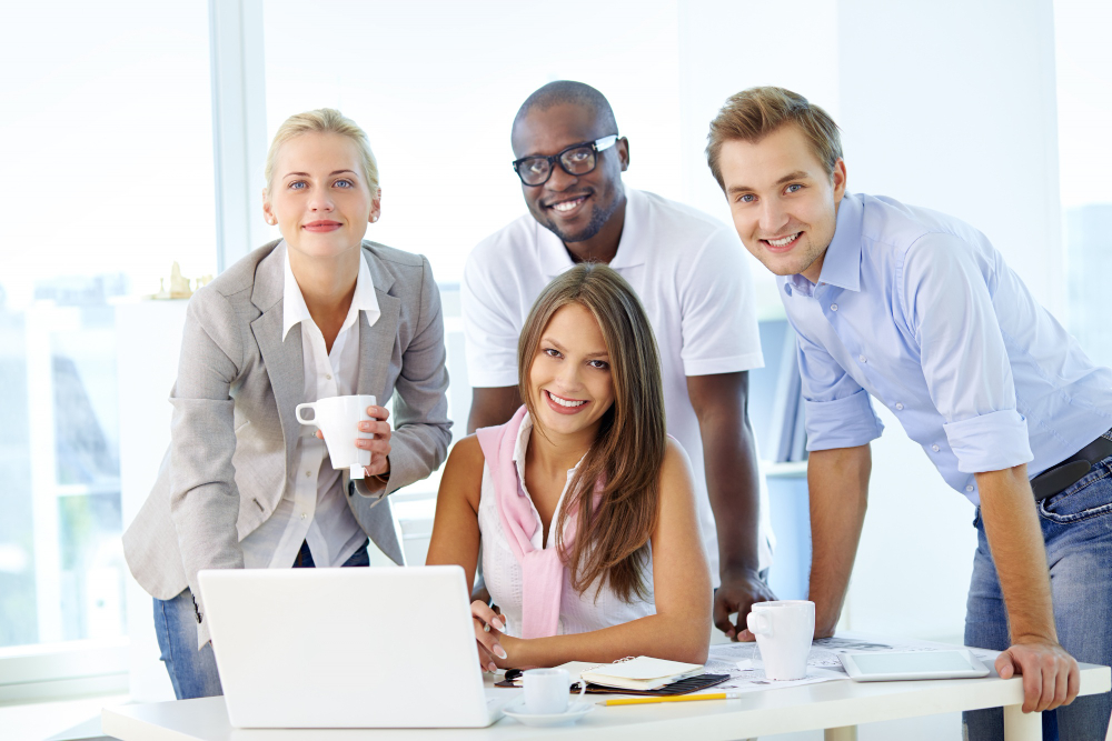 people gathered around a laptop, smiling at the camera