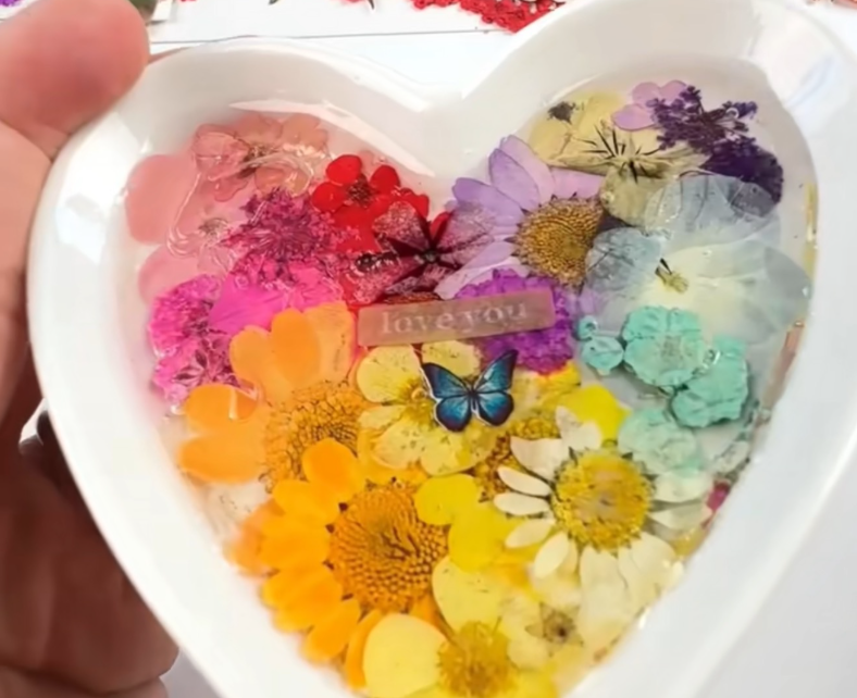 A heart-shaped ring dish full of flowers and decorative stamps.